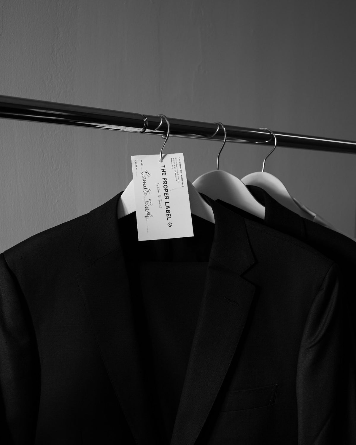 Two black jackets on white hangers beneath a named fitting tag. Maison de Sport — Collection 005. Photography: Malike Sidibé, New York.