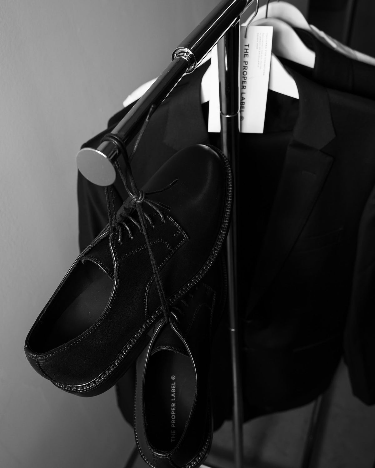 Historical black lace-up shoes beside a tailored jacket on a clothing rail. Maison de Sport — Collection 005. Photography: Malike Sidibé, New York.