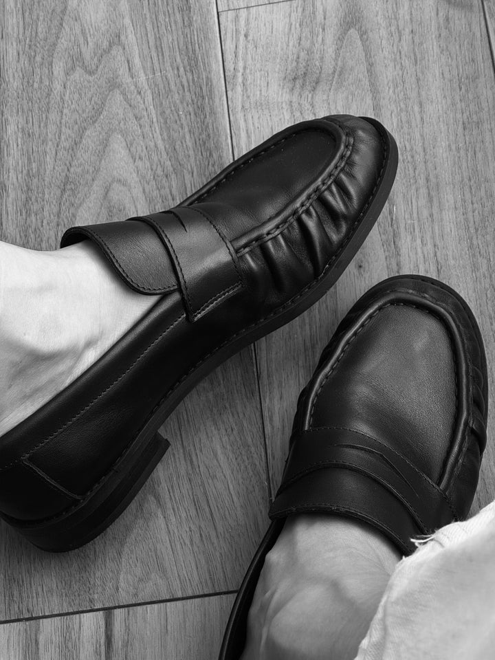 Black-and-white photograph of The Proper Moccasin worn on a wooden floor.