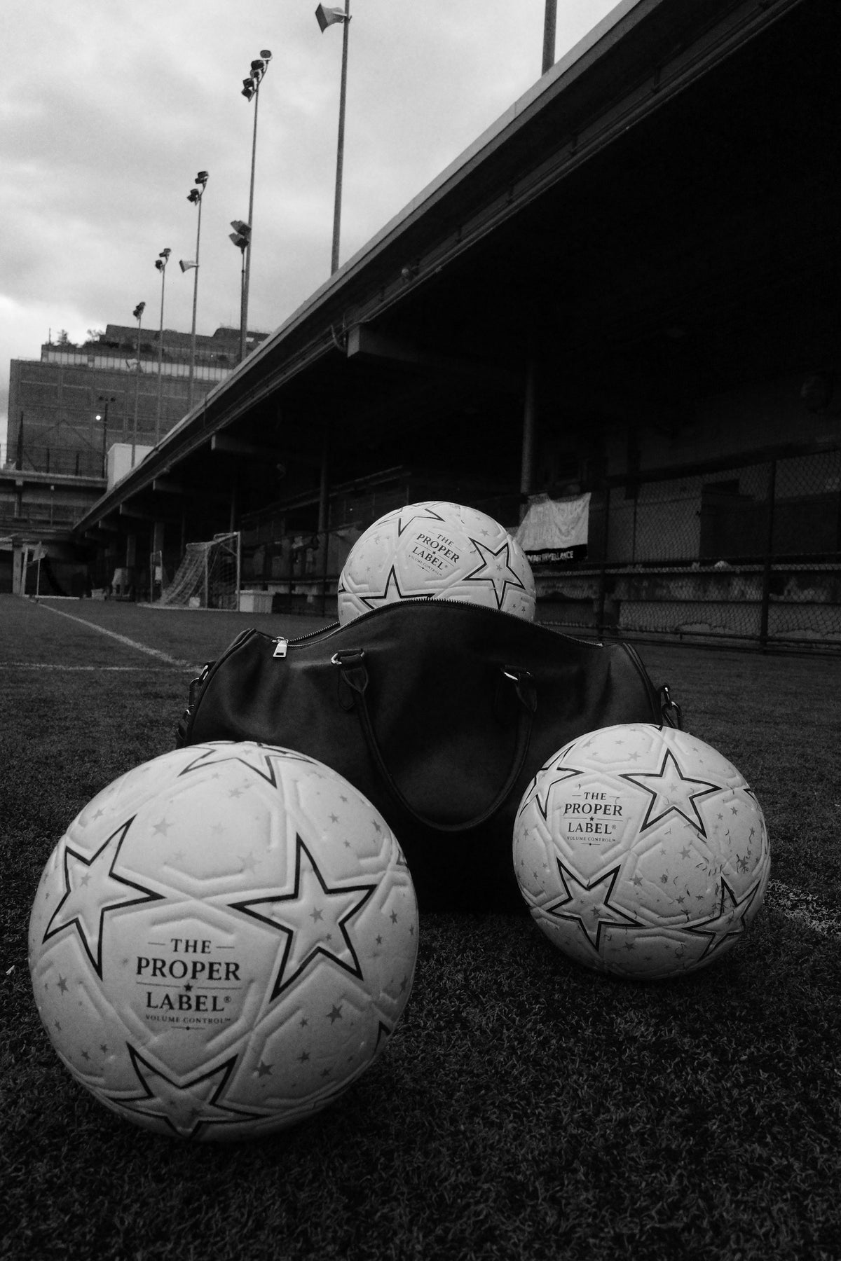 Three The Proper Label footballs and a black leather travel bag on the urban pitch
