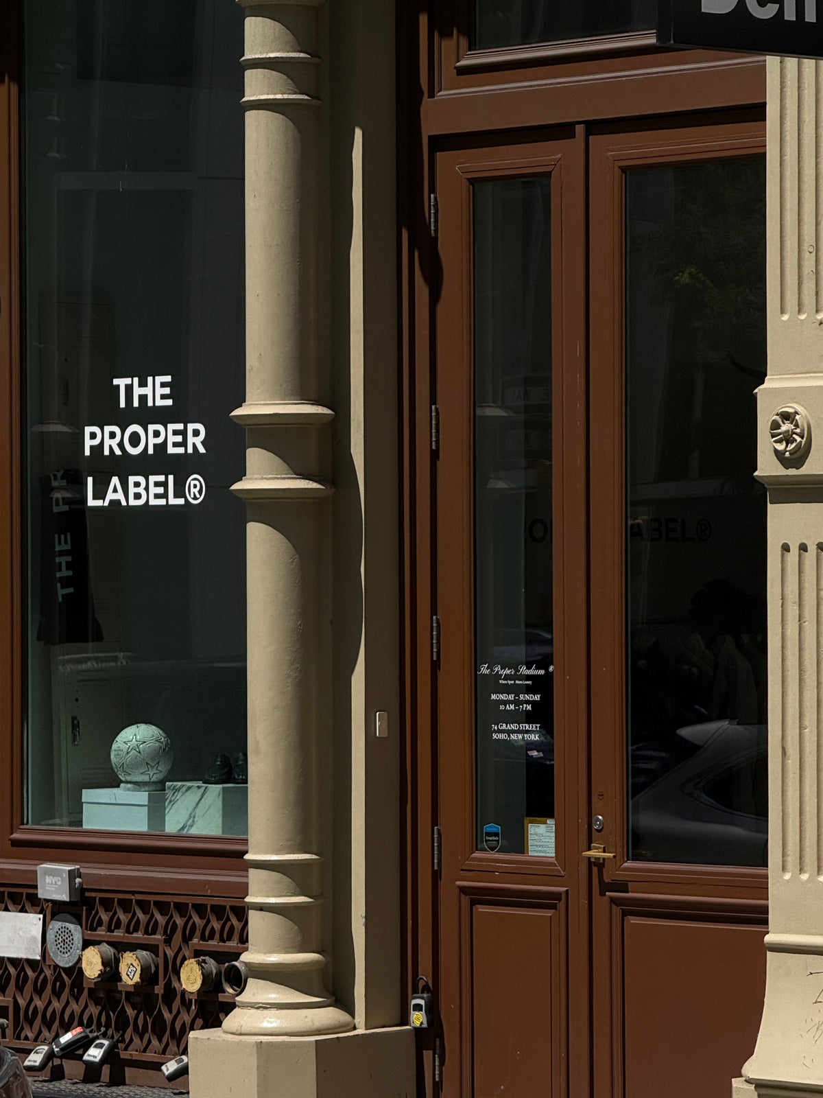 The Proper Stadium entrance and window at 74 Grand Street, with the Proper Label signature and a football displayed inside.