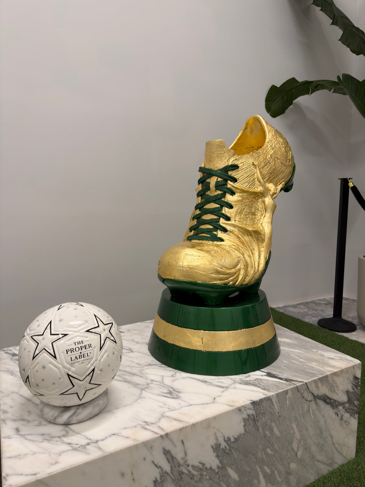 A gold football boot sculpture and The Proper Label football on a marble plinth
