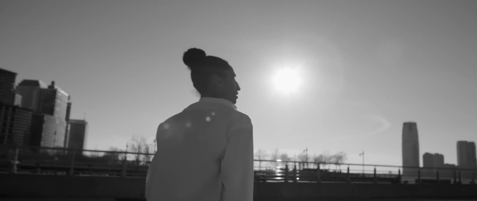 Une silhouette en chemise blanche, de profil, devant le soleil et la skyline au bord de l’eau.
