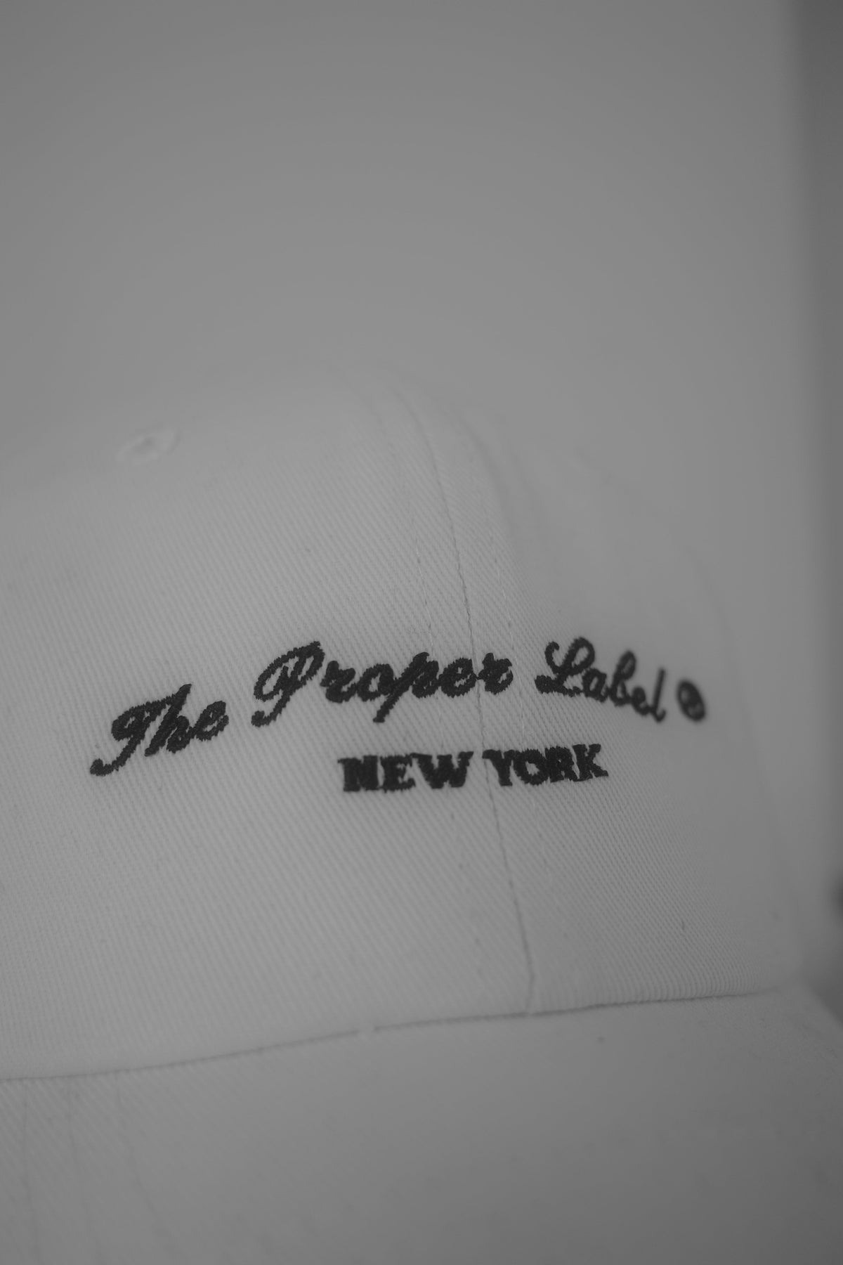 The Proper Label New York embroidered in black on a white cap.