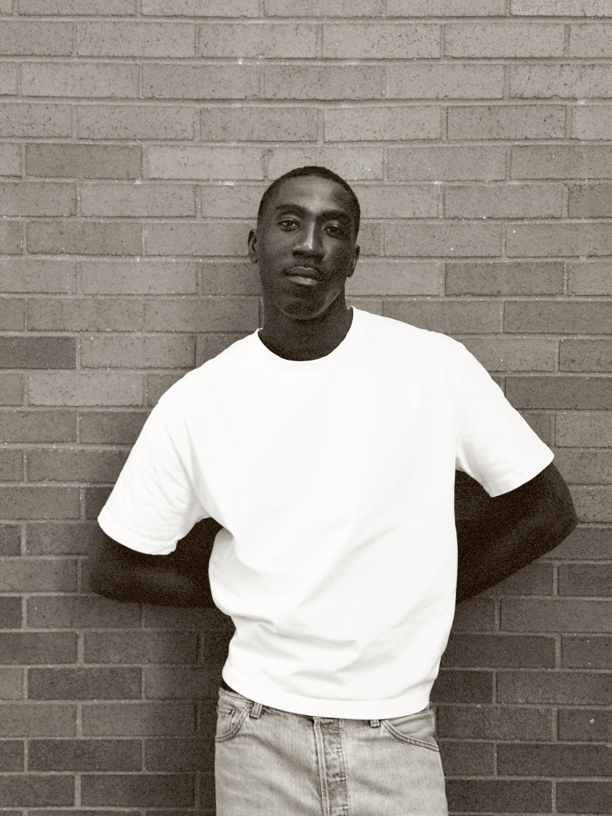 Camille Tanoh, founder of The Proper Label, wearing a white T-shirt against a brick wall.