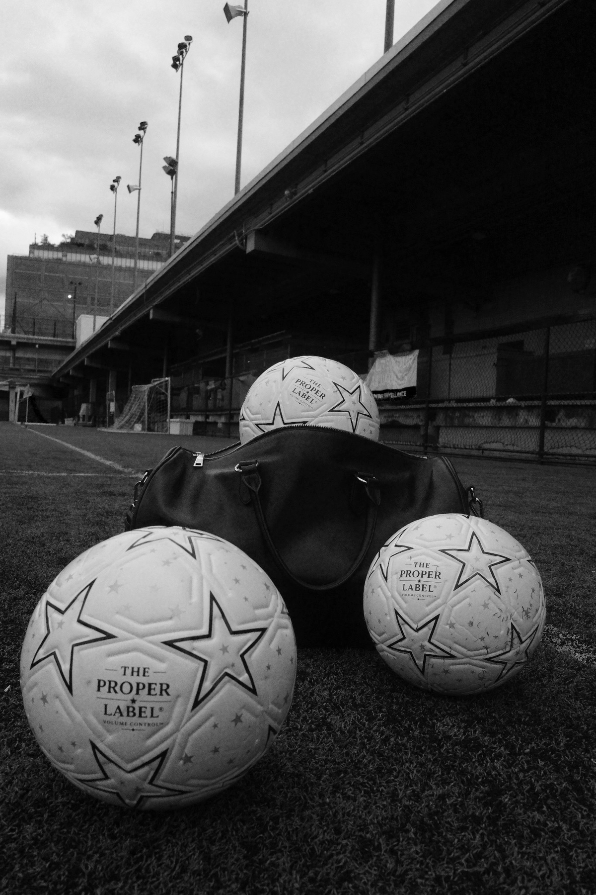 Three Proper Starballs arranged around a black travel bag on the pitch, photographed in black and white.