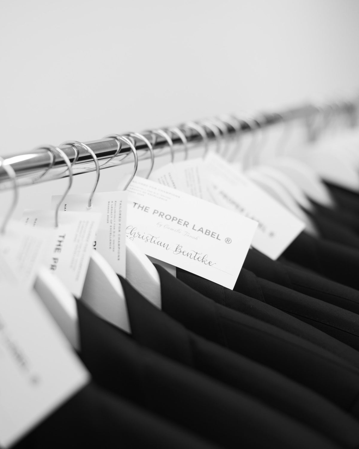 Black-and-white view of jackets and Christian Benteke’s name tag on a clothing rail. Maison de Sport — Collection 005. Photography: Malike Sidibé, New York.