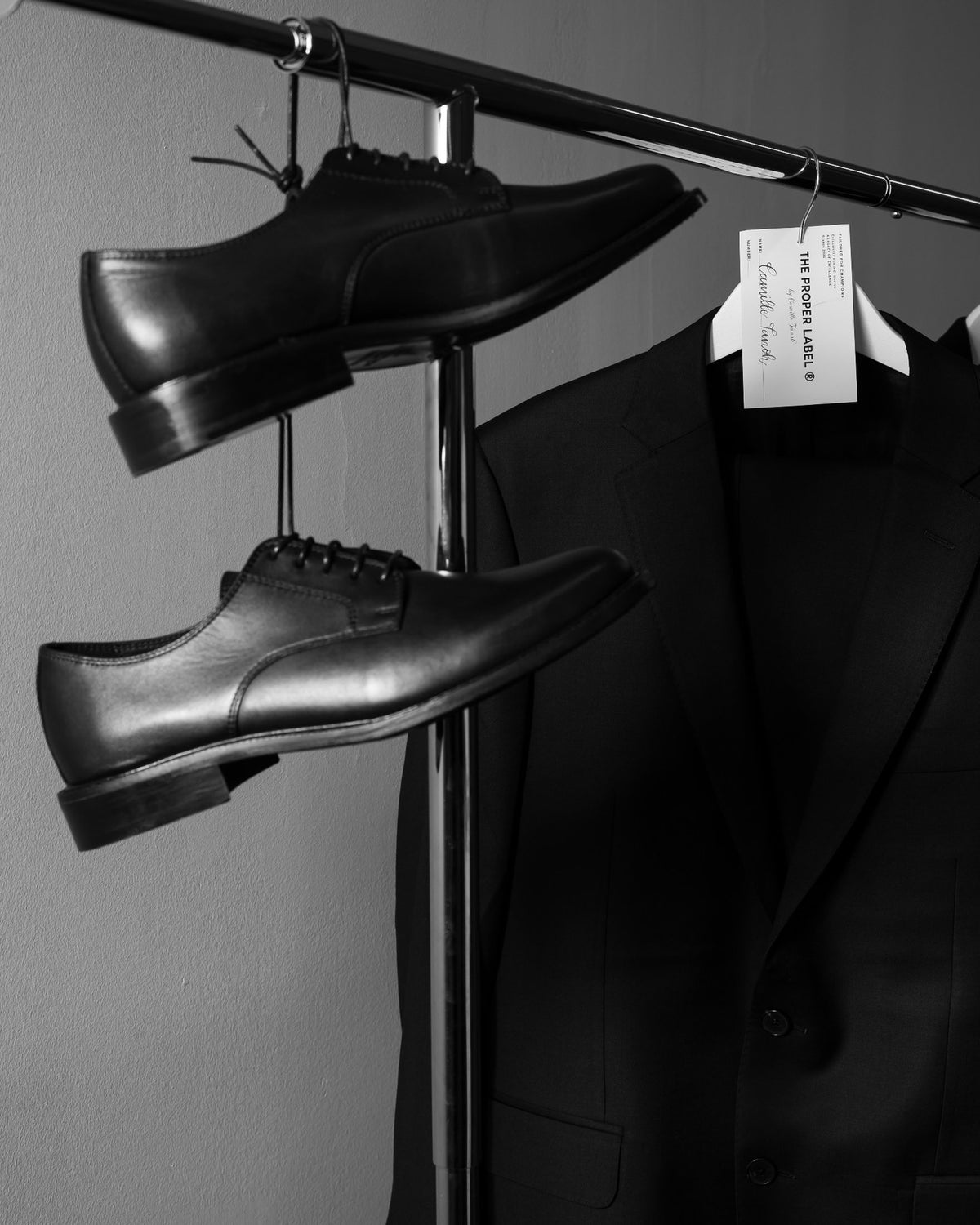 Historical lace-up shoes in profile, hanging beside a tailored jacket. Maison de Sport — Collection 005. Photography: Malike Sidibé, New York.
