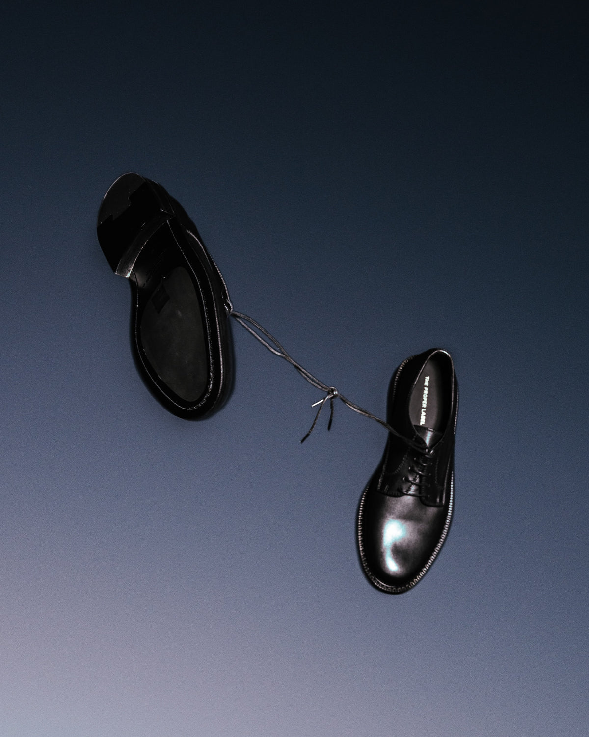 Deux Derby en cuir noir poli suspendus par leurs lacets.