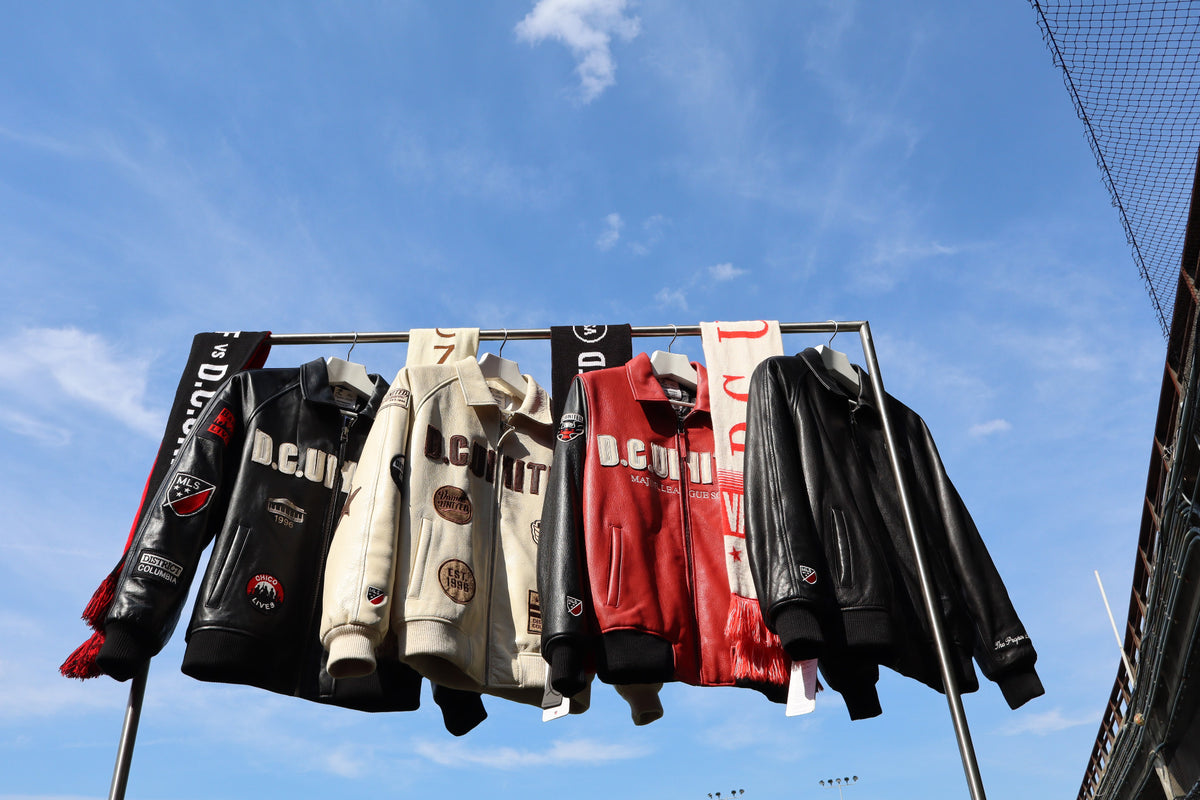 Four D.C. United leather jackets and scarves hanging on a clothing rail against a blue sky.