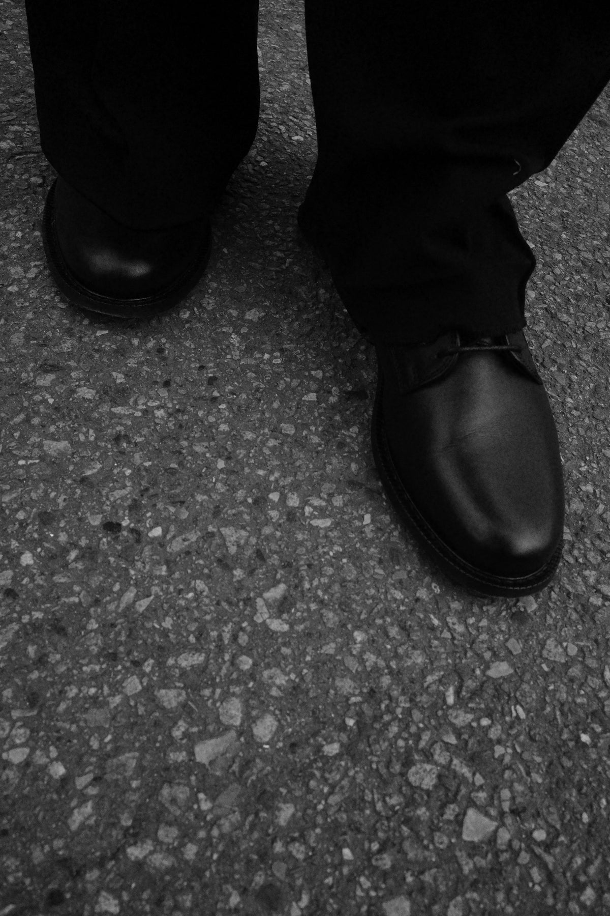Black Legacy Derby shoes worn with dark trousers on textured pavement.