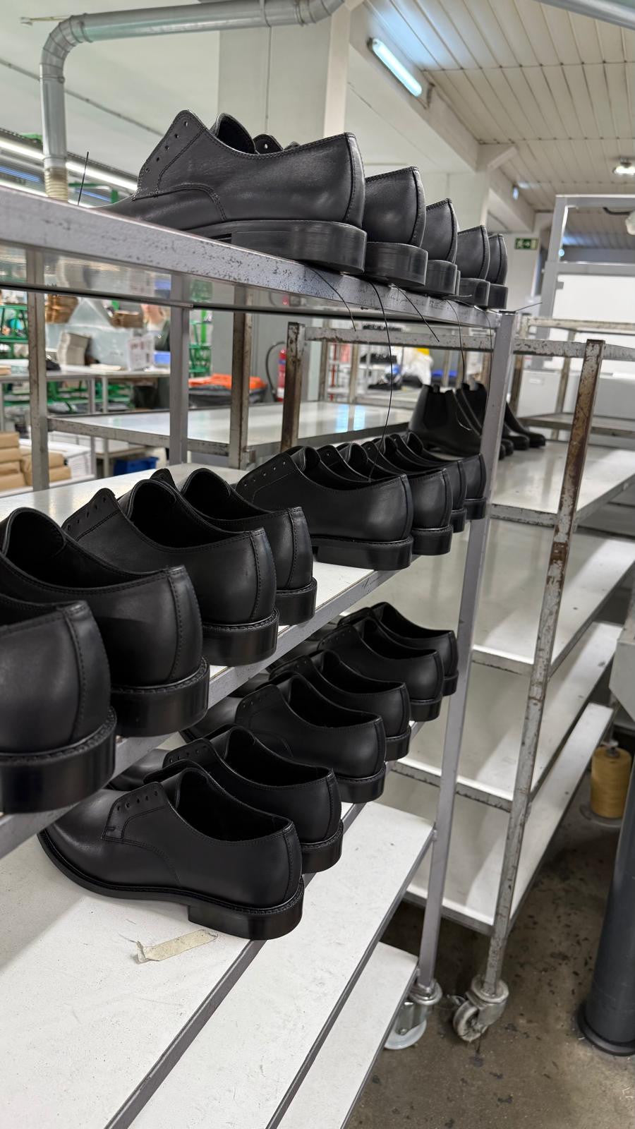 Black leather Legacy Derby shoes awaiting laces on a production rack in the workshop.