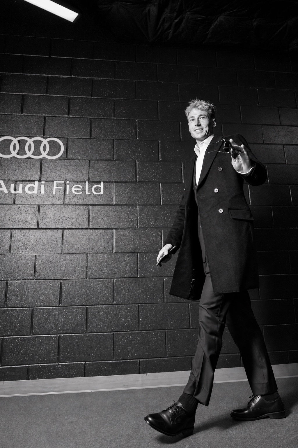 Lukas MacNaughton wearing a dark overcoat, white shirt, tailored trousers and black Derby shoes at Audi Field.