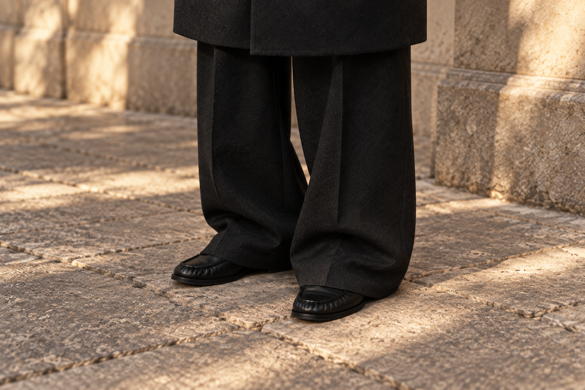 The Proper Moccasin beneath oversized black tailored trousers, with only the low supple toes showing.
