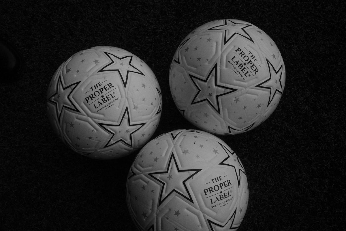 Three white Proper Starball footballs on a dark football pitch, in black and white.