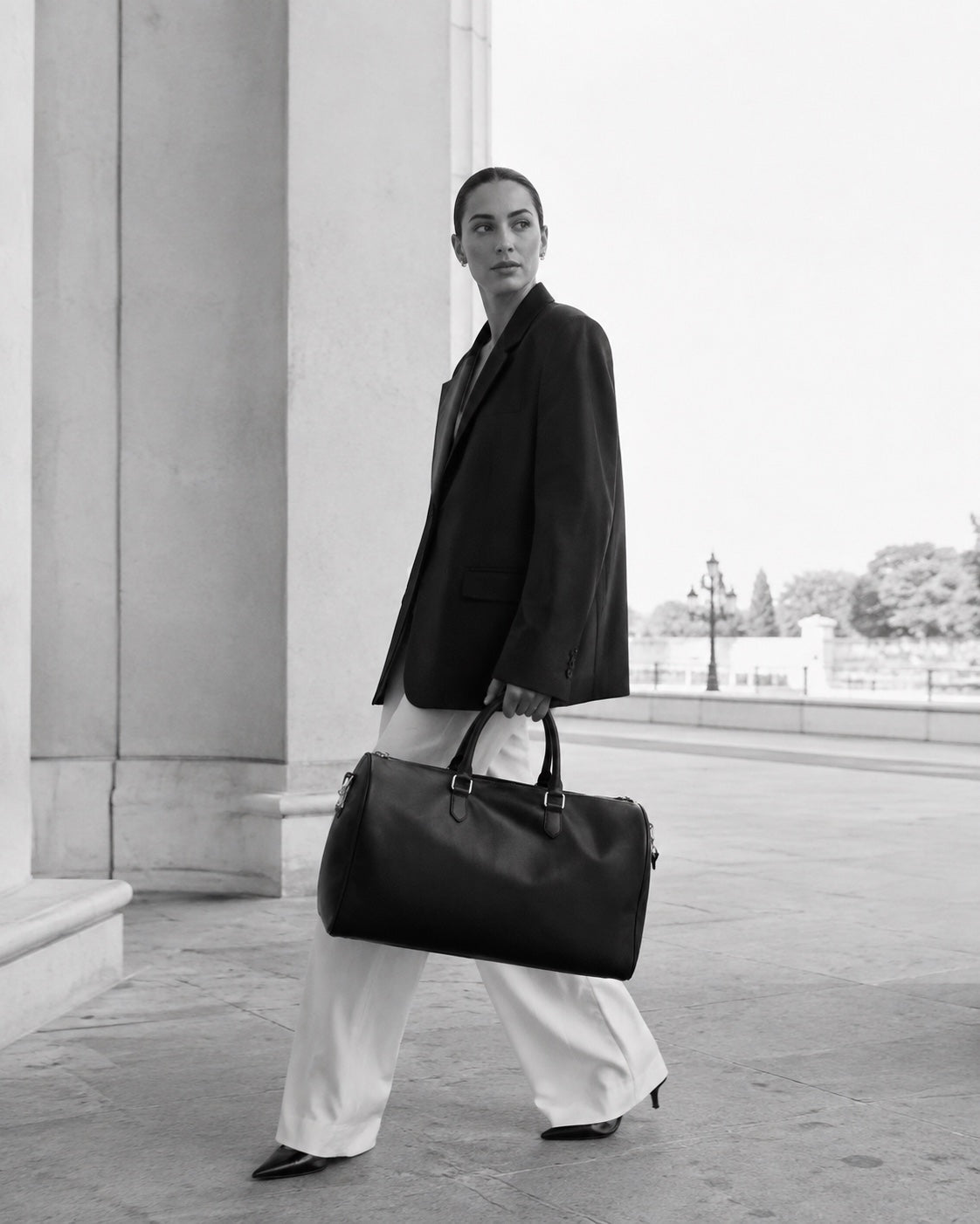 Editorial photograph of a woman carrying The Continental Holdall beneath a city portico — The Proper Label.
