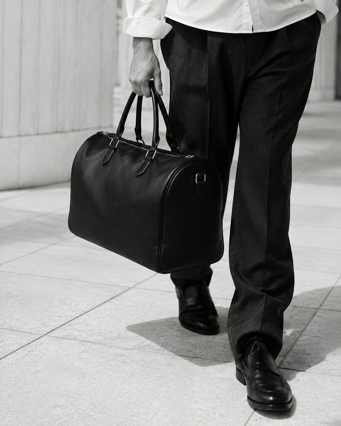 The Continental Holdall carried through a stone corridor, with tailored trousers and loafers — The Proper Label.
