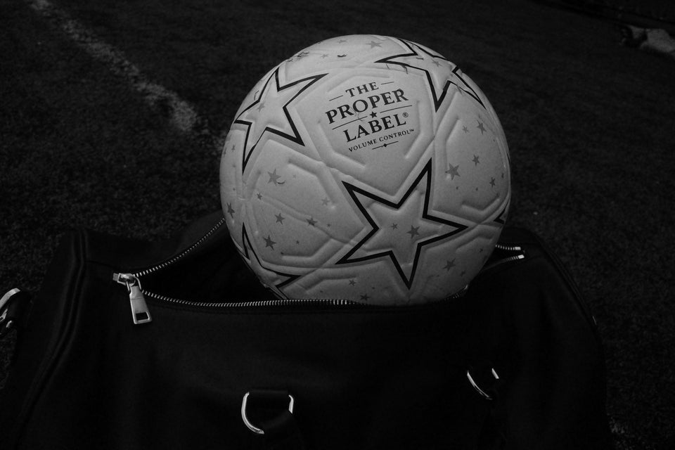 The Proper Label football resting in a black leather travel bag on the pitch