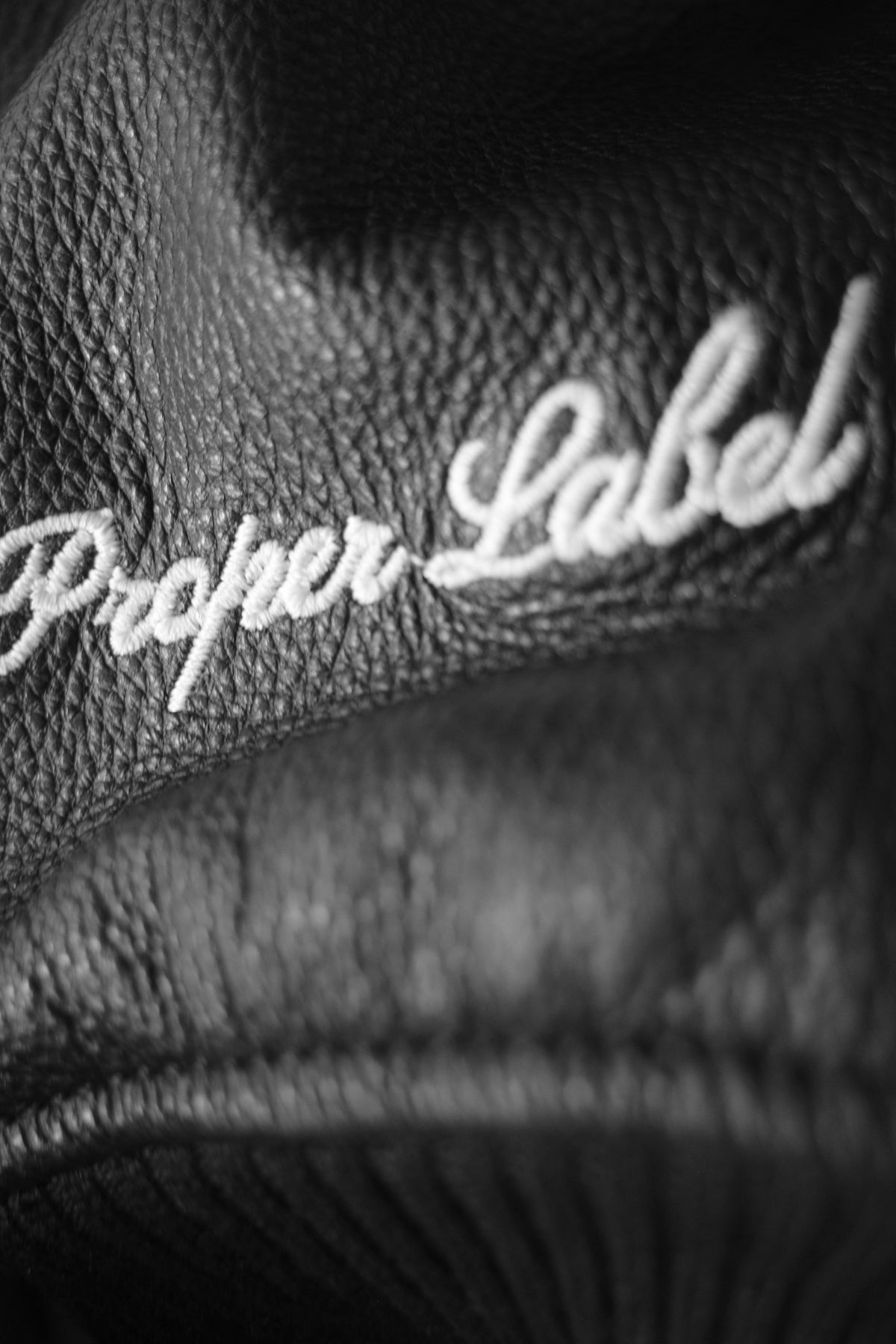 Close-up of The Proper Label signature embroidered on grained black leather