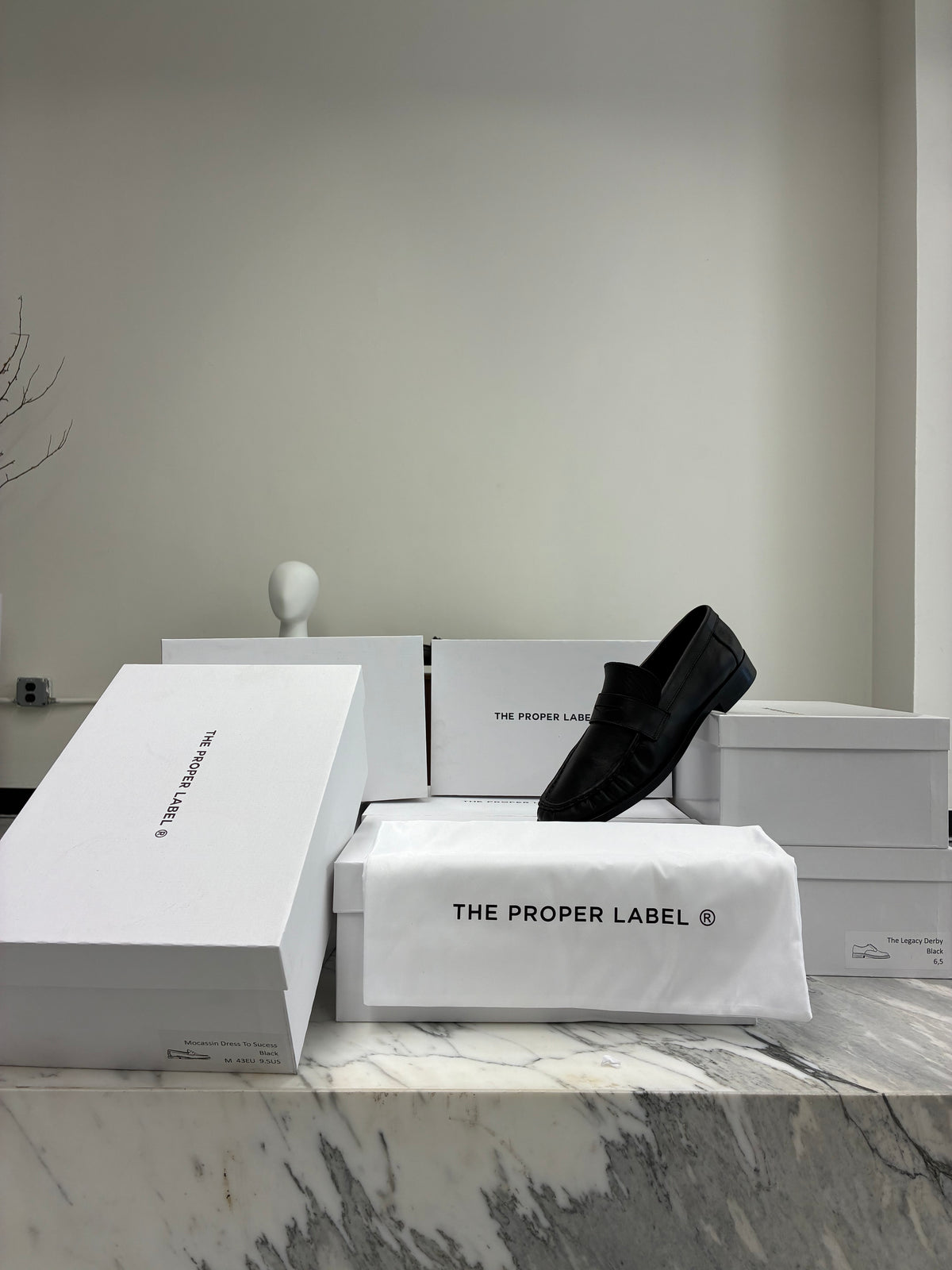 The Proper Moccasin with white boxes and a dust bag on a marble counter