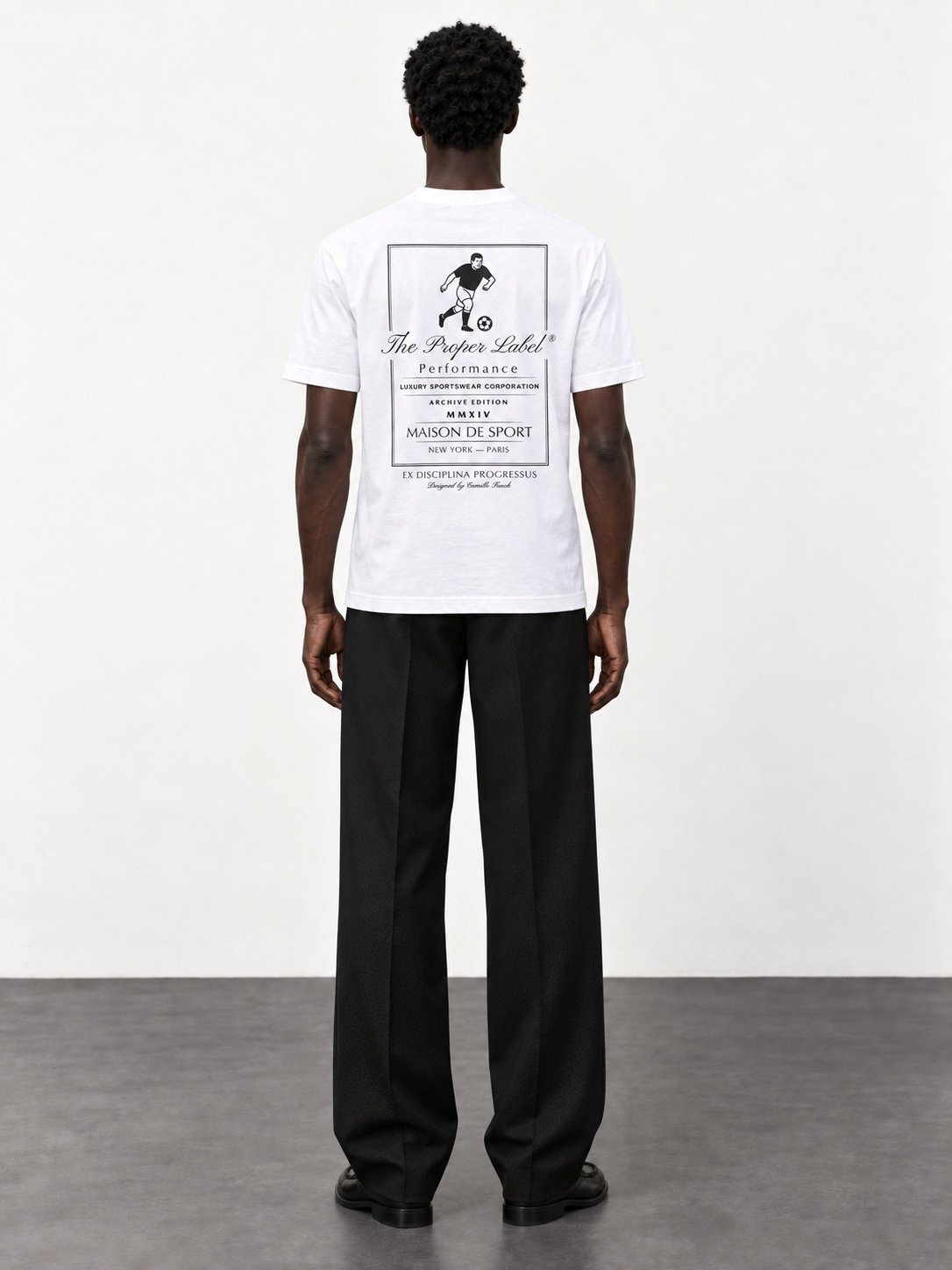 Maison de Sport white T-shirt — back studio view with black tailored trousers and moccasins.