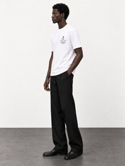 Maison de Sport white T-shirt — side studio view with black tailored trousers and moccasins.