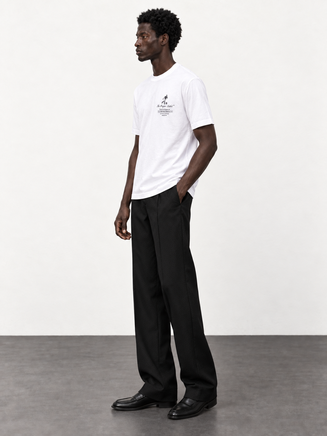 Maison de Sport white T-shirt — side studio view with black tailored trousers and moccasins.