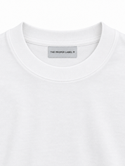 Studio close-up of the white ribbed crew neck, cotton and single The Proper Label woven label.