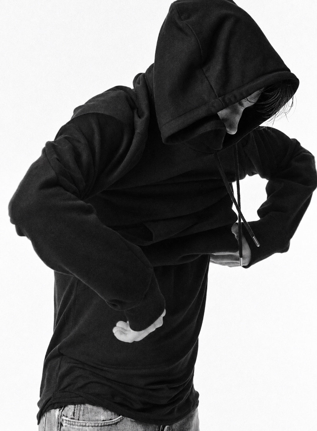 A model pulling on a black Proper Essentials hoodie, photographed in black and white