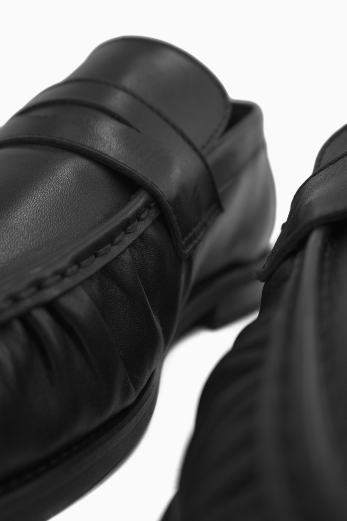 Close-up of The Proper Moccasin in black calf leather, showing the saddle and gathered apron seam.
