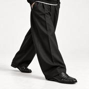 The Proper Moccasin® — Obsidian Black, an open stride beneath wide black trousers.