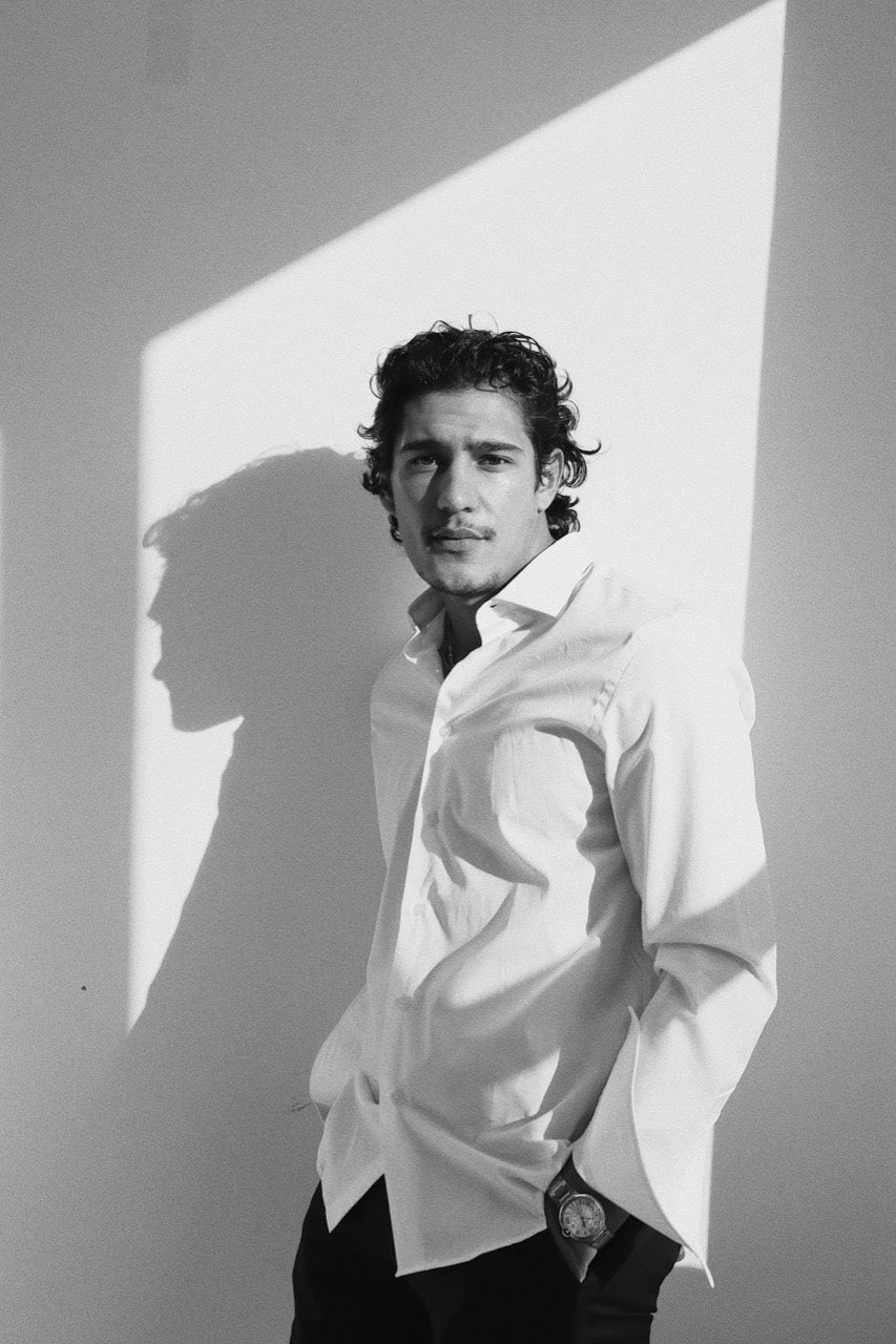 Gabriel Robles in a white shirt, standing in a shaft of sunlight beside a wall.
