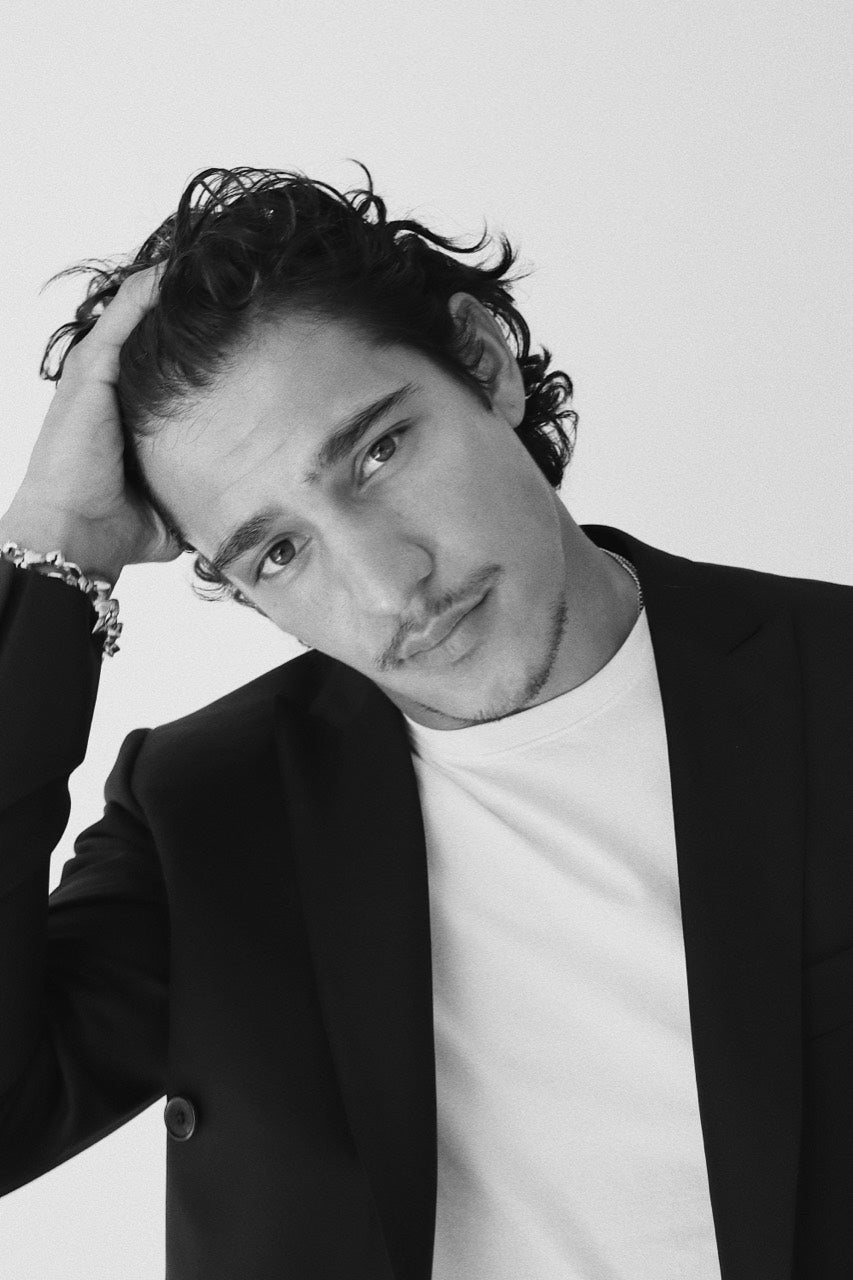 Close portrait of Gabriel Robles in a black jacket and white T-shirt, with a hand in the hair.
