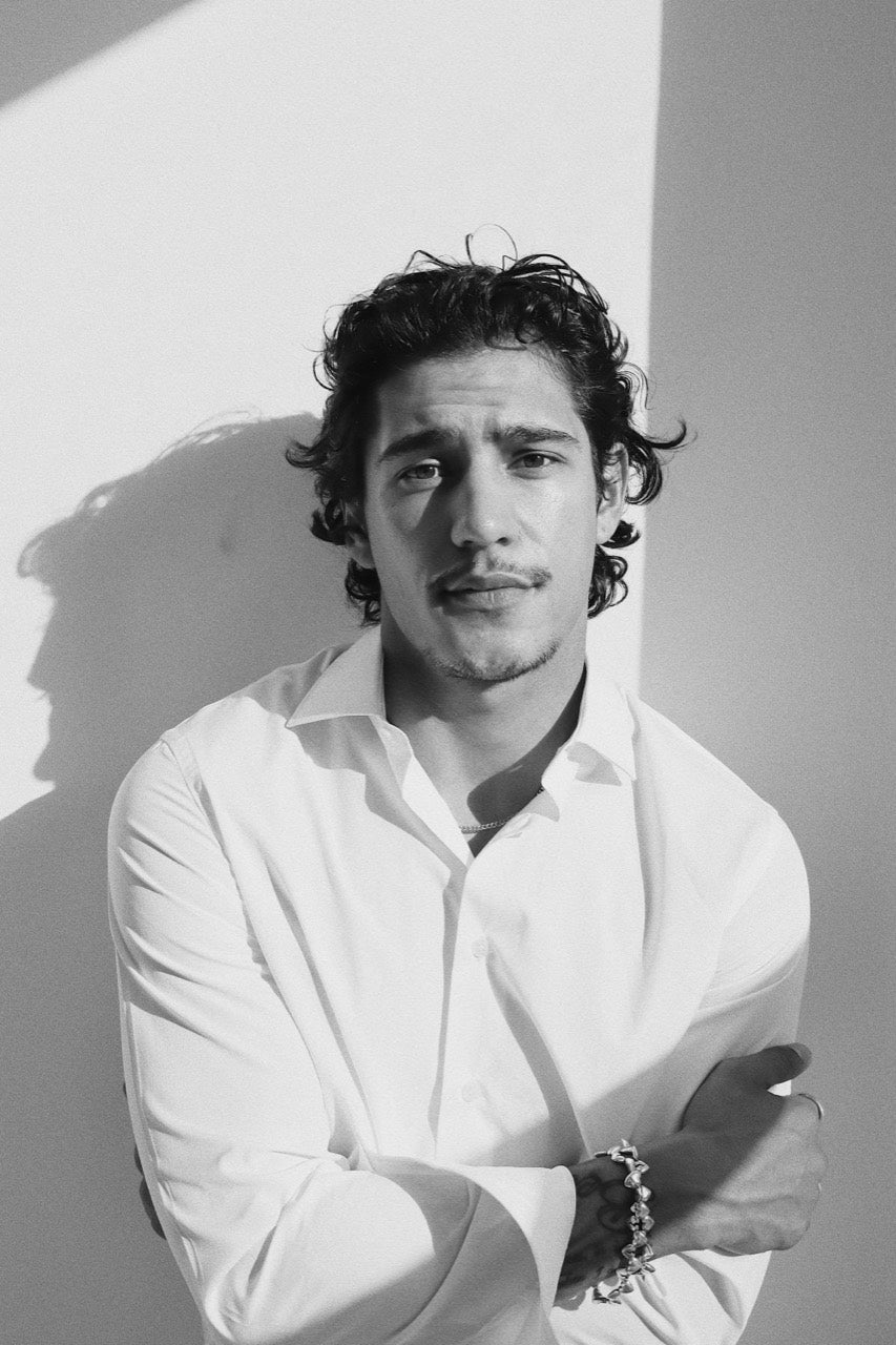 Gabriel Robles in a white shirt with arms crossed, framed by light and shadow.