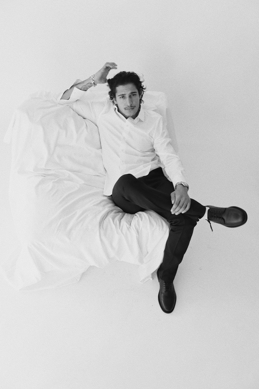 Gabriel Robles seated with legs crossed in a white chair, wearing black lace-up shoes.