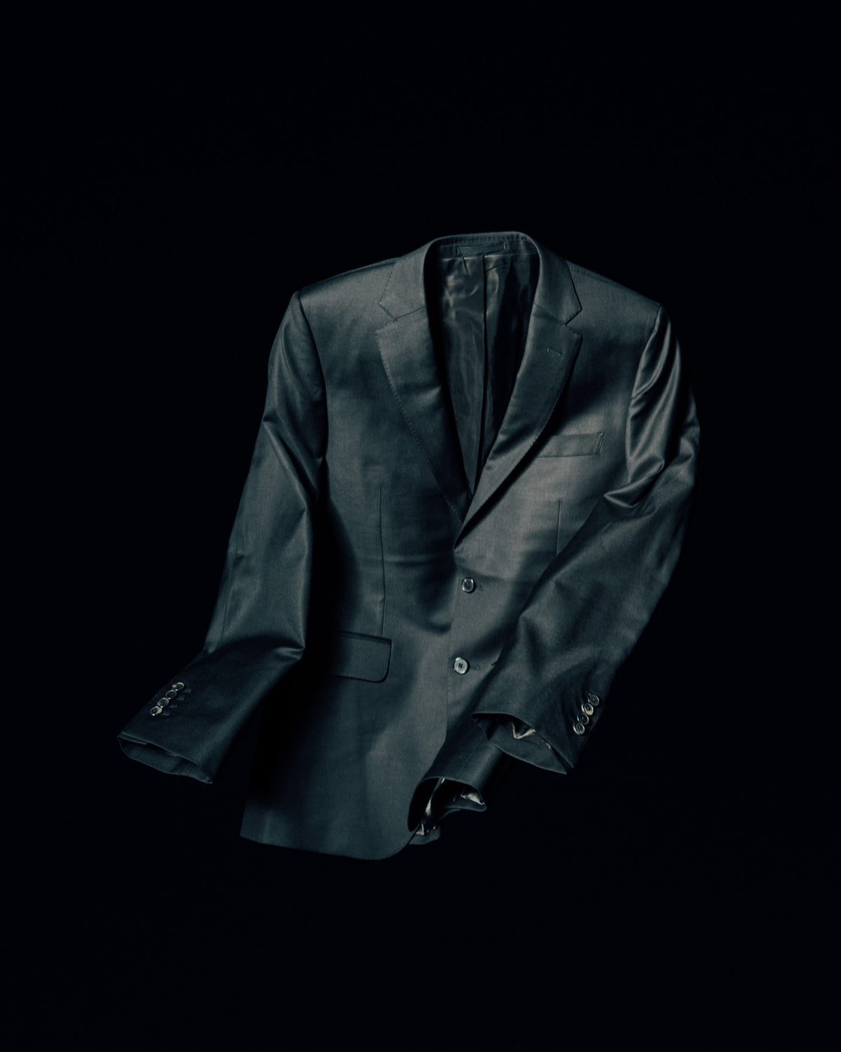 A dark single-breasted blazer held in a sculptural shape against a black background.