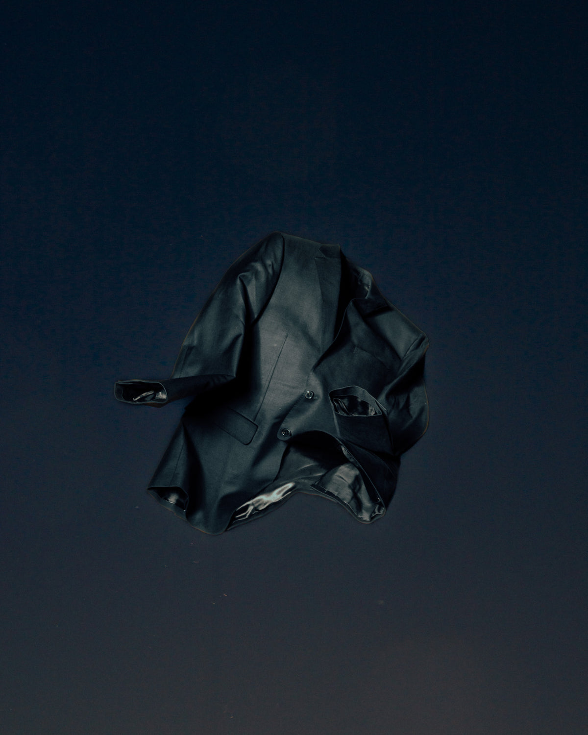 A dark blazer shown at an angle, its sleeves and hem folding away from the body.