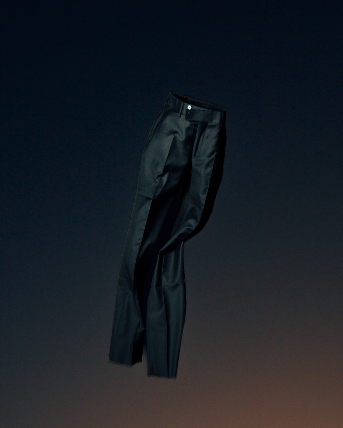 Dark tailored trousers suspended at a slight angle, showing the waistband and full length.