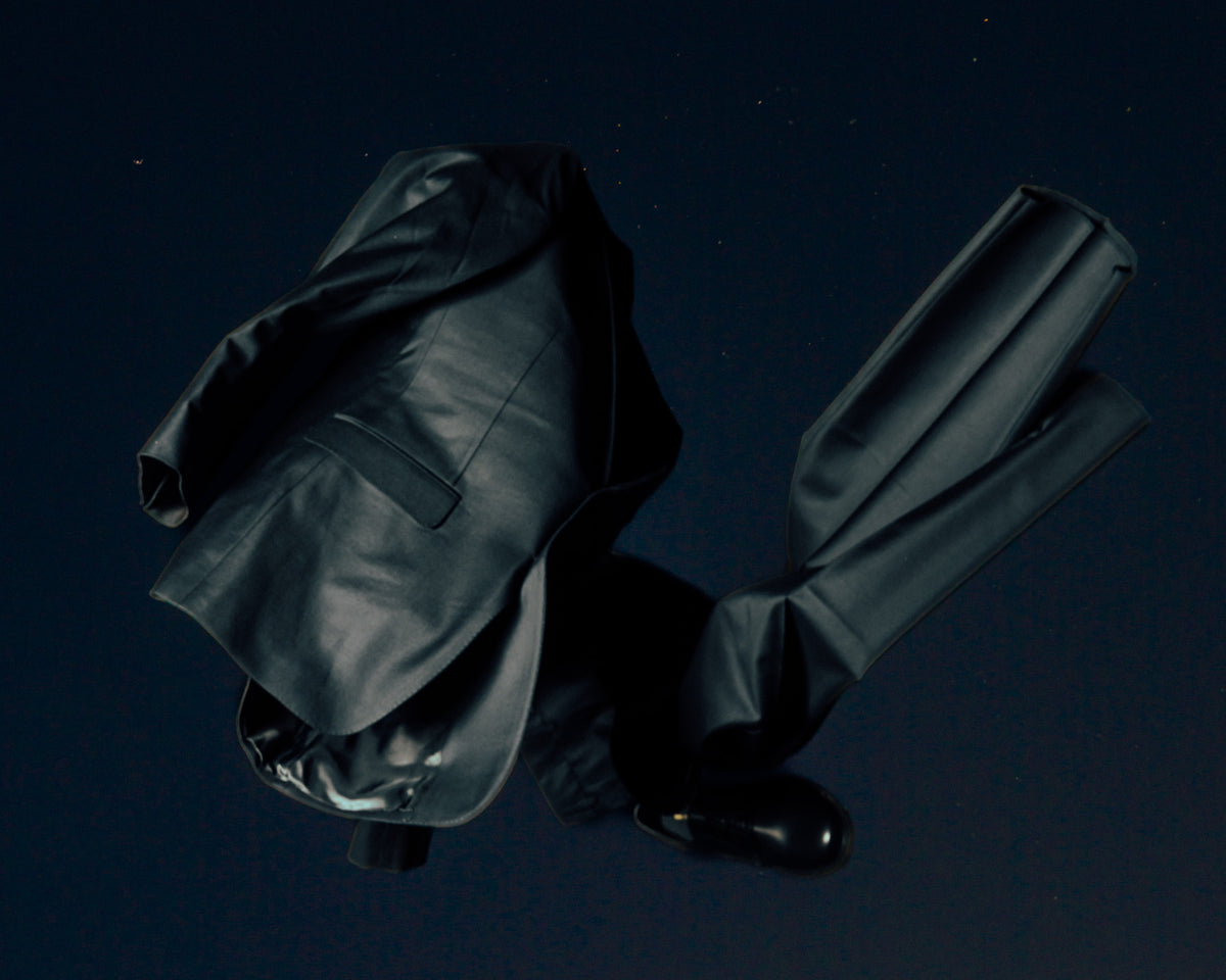 A dark blazer, trousers and black shoe arranged as a floating silhouette.
