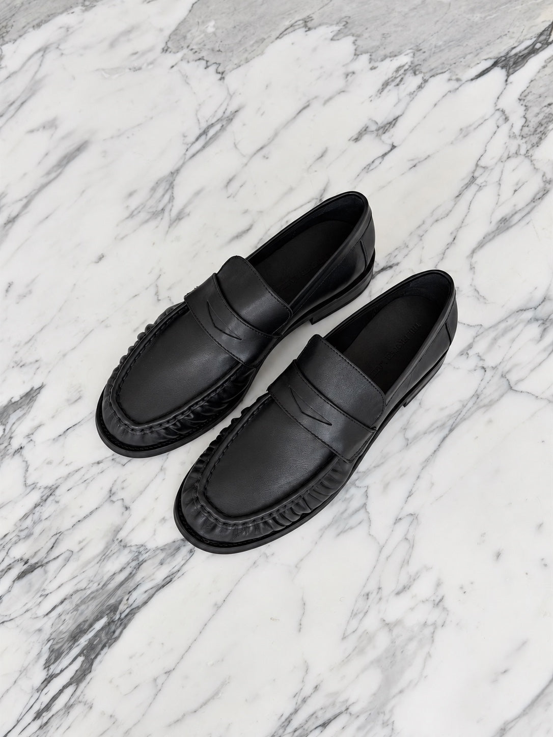 Black The Proper Label loafers on veined white marble.