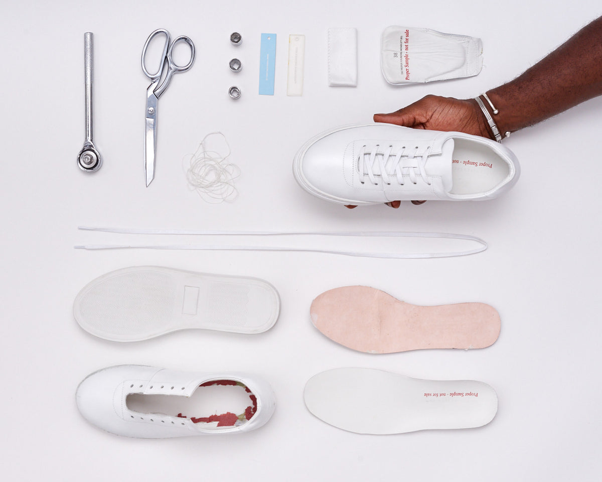 White sneaker sample held above its laid-out components, laces and tools.