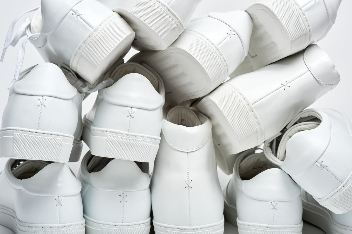 White sneakers arranged together, showing heel seams, soles and stitching.