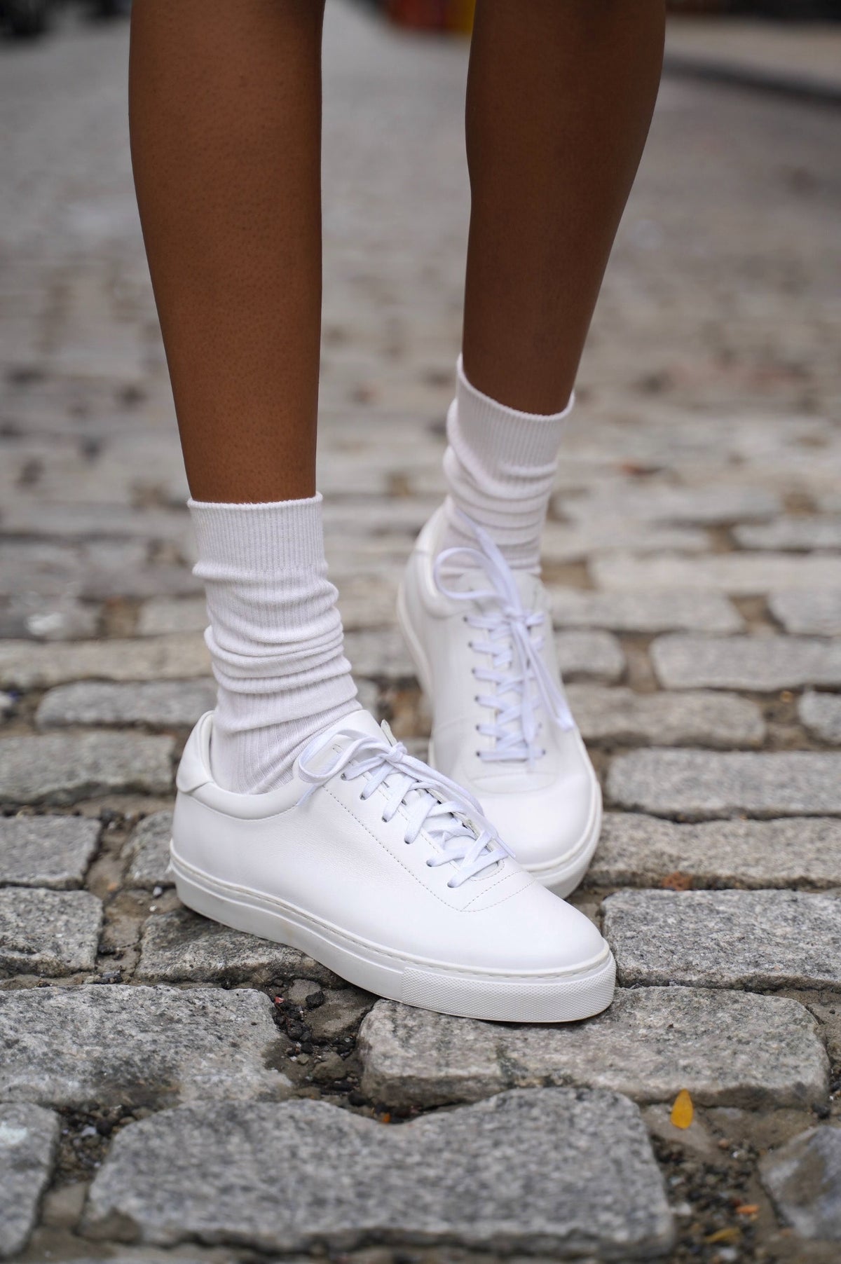 Close view of white sneakers and white socks on a cobbled surface.