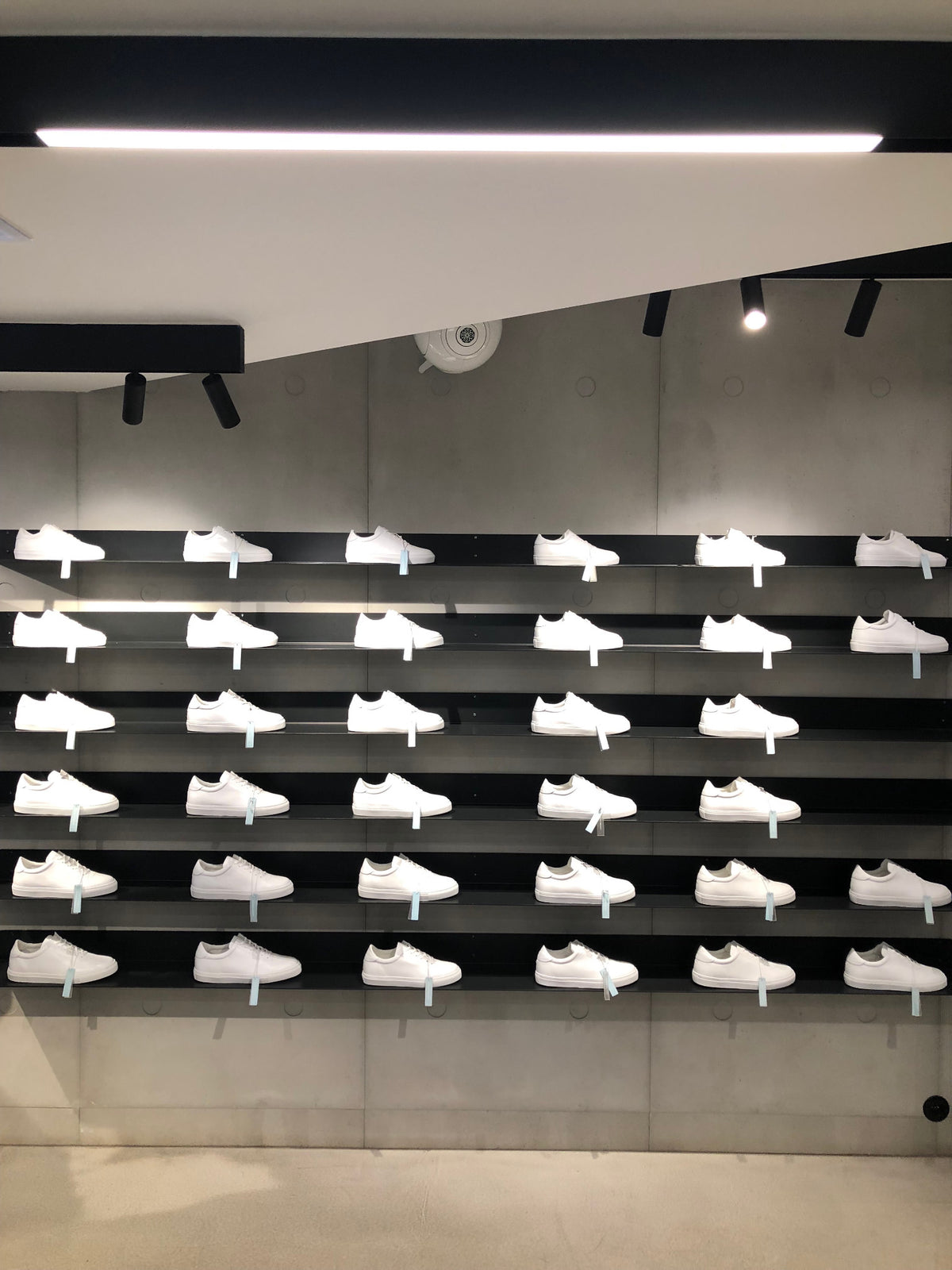 Rows of white sneakers arranged on black wall-mounted shelves.
