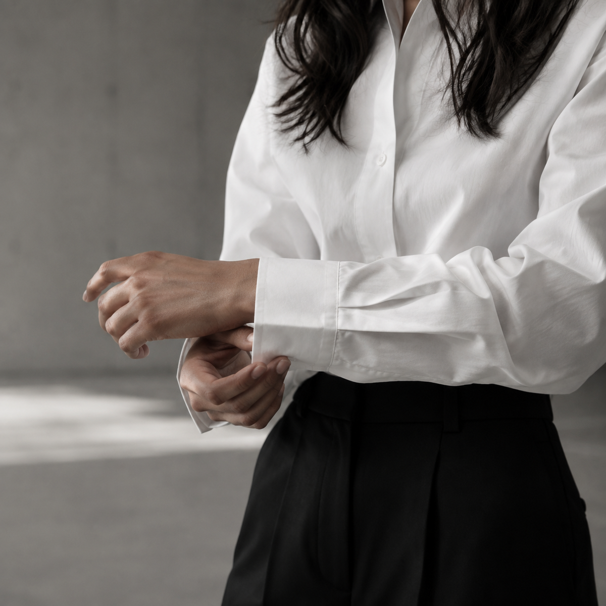 Close study of a woman adjusting the cuff of her white cotton shirt.