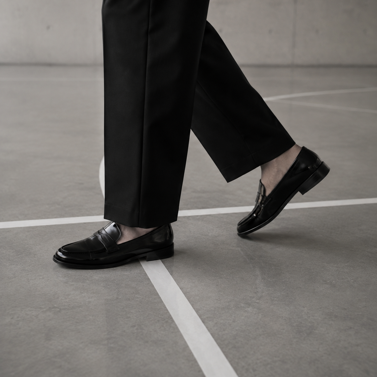 Black penny loafers and tailored trouser hems crossing a white court line.