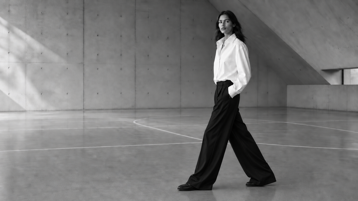 A woman in a white poplin shirt and long wide black trousers, wearing The Proper Moccasin.