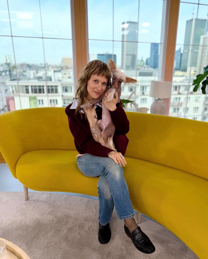 A woman seated on a yellow sofa with a small dog, wearing jeans and black leather moccasins.