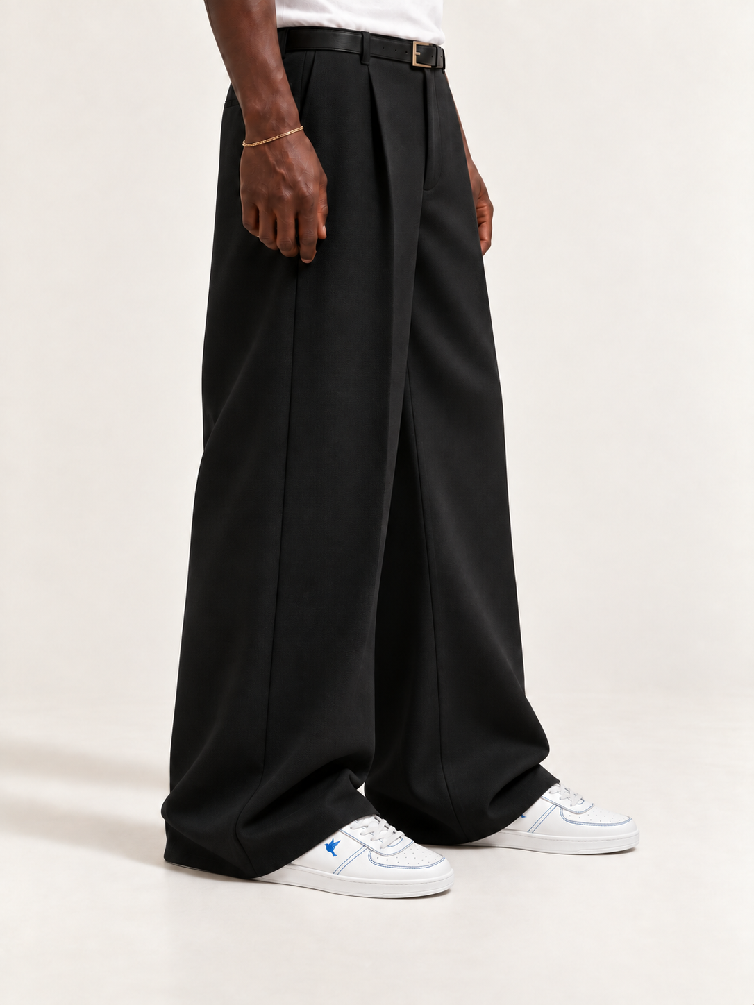 The Proper Fly Sneaker — White / Blue, worn with long black trousers, a tucked white T-shirt, a slim belt and discreet gold-tone accessories.