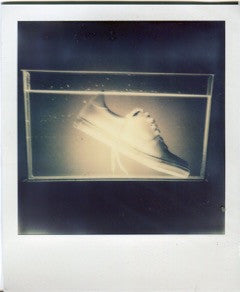 Polaroid of a white sneaker seen through a rectangular glass tank.